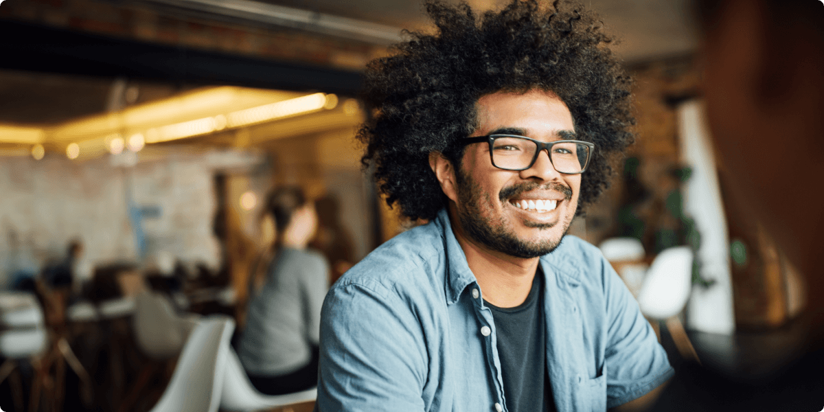 Um homem de óculos dá um sorriso largo em um café.